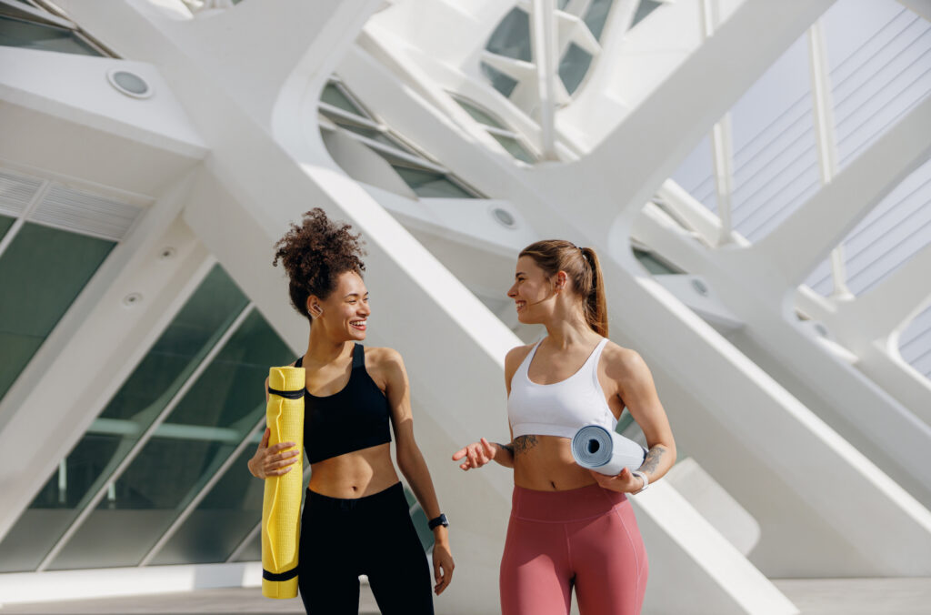 Two young fit women walking in the city with their yoga mats after doing morning workout